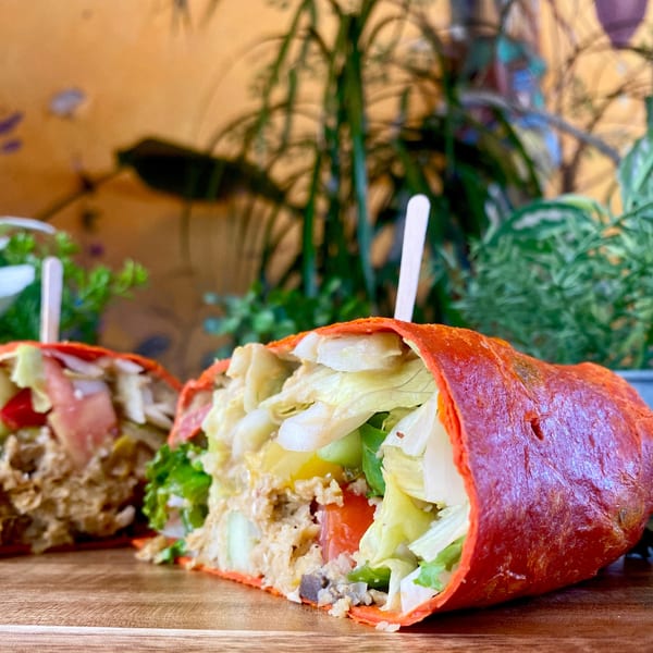 Two halves of a red tortilla wrap filled with chicken salad, lettuce, and tomatoes on a wooden board.