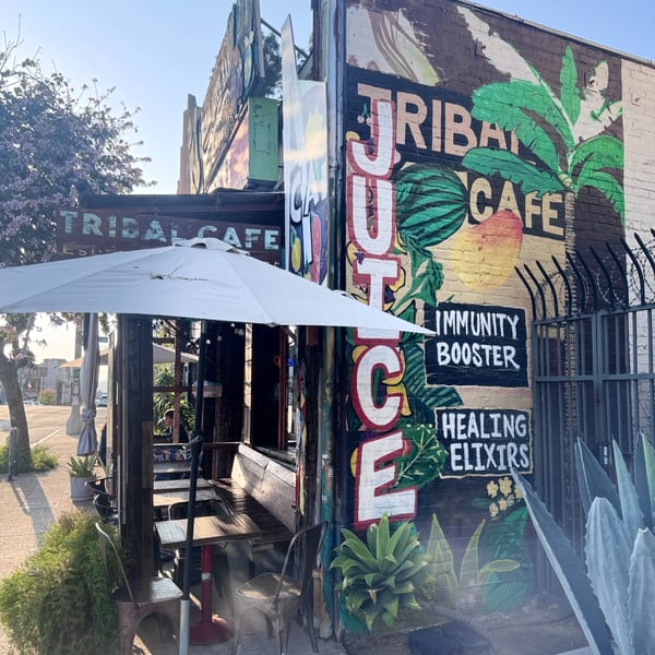 Exterior of Tribal Cafe with a colorful mural, outdoor seating, and a white umbrella.