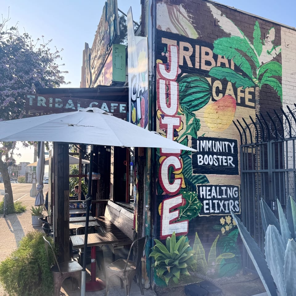 Exterior of Tribal Cafe with a colorful mural, outdoor seating, and a white umbrella.