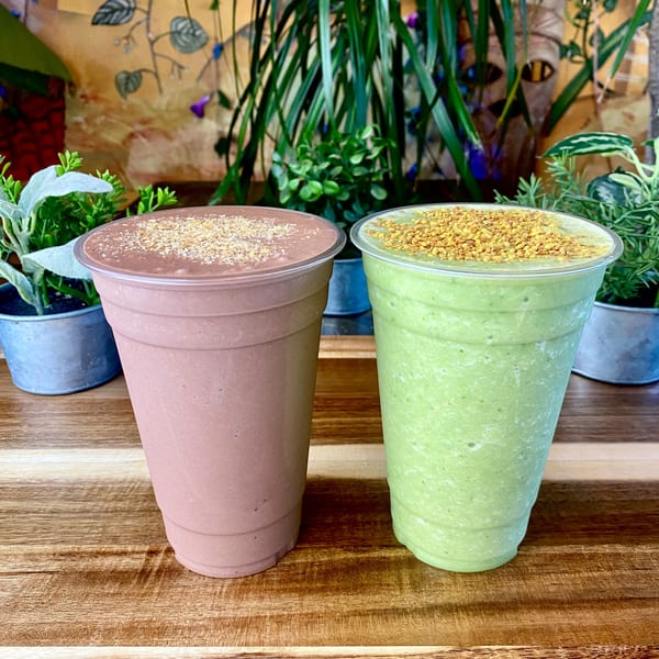 Two Tribal Cafe smoothies, one chocolate and one green, topped with granola, on a wooden table.