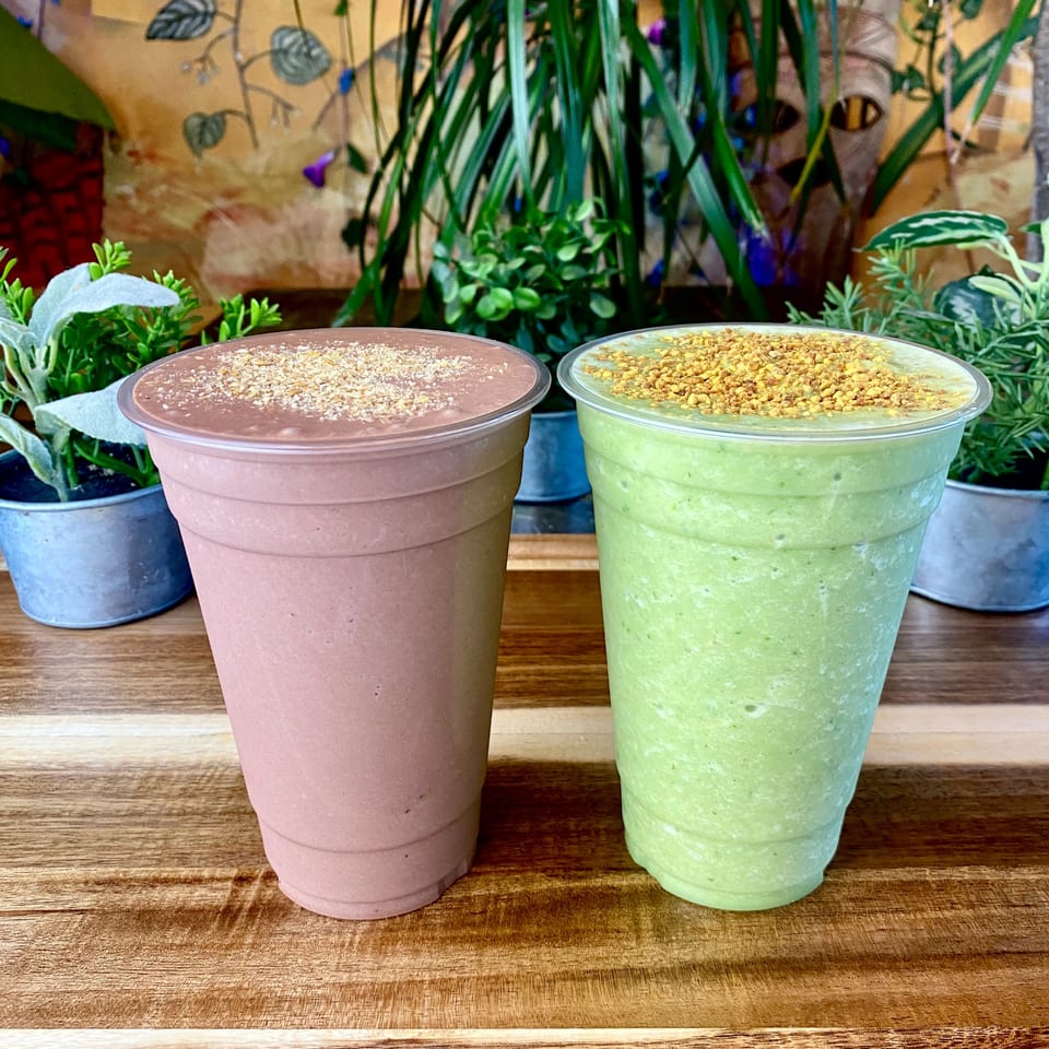 Two Tribal Cafe smoothies, one chocolate and one green, topped with granola, on a wooden table.