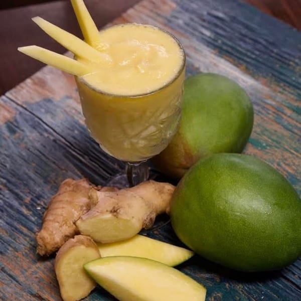 Mango smoothie with mango slices and ginger on a rustic wooden surface at Tribal Cafe.