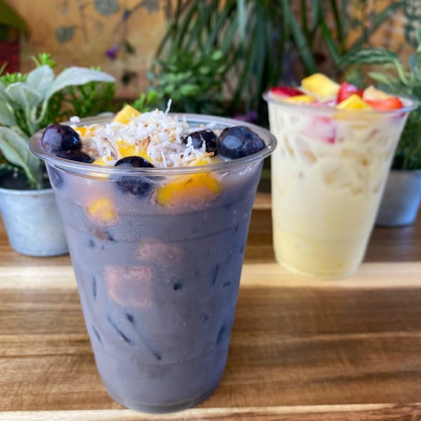 Two Tribal Cafe fruit drinks, one purple with blueberries and coconut, one yellow with mixed fruit.