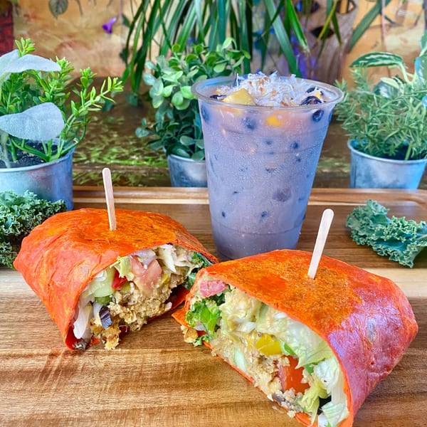 A Tribal Cafe wrap, cut in half, with a drink, on a wooden board with plants.
