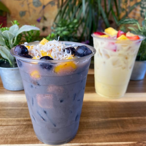 Two colorful fruit drinks on a wooden table, one purple with blueberries and mango, the other yellow with fruit.