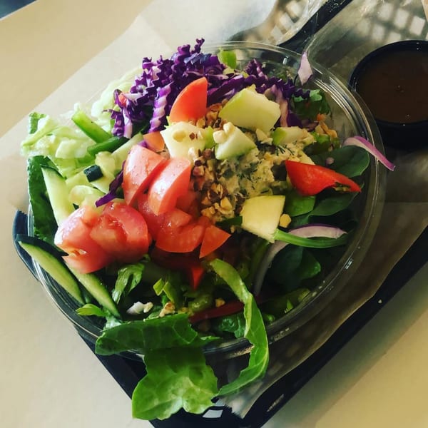 A vibrant Tribal Cafe salad with tomatoes, purple cabbage, green apples, and nuts, with dressing on the side.