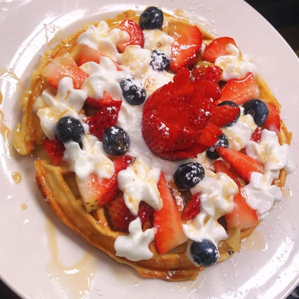 Golden waffle topped with whipped cream, fresh strawberries, blueberries, and a drizzle of syrup.