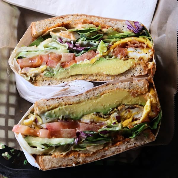 Two halves of a Tribal Cafe sandwich, filled with avocado, egg, bacon, lettuce, and tomatoes.