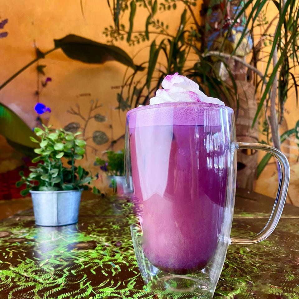 A vibrant purple drink with whipped cream in a clear mug on a green patterned table at Tribal Cafe.