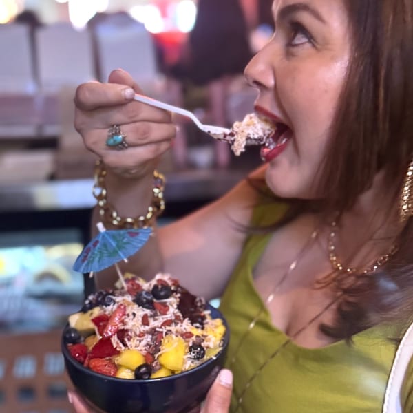 A woman in a green top enjoys a colorful fruit bowl with a tiny umbrella at Tribal Cafe.
