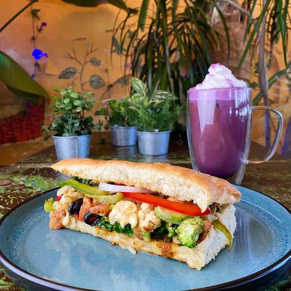 A Tribal Cafe sandwich with vegetables and olives, alongside a purple drink with whipped cream.