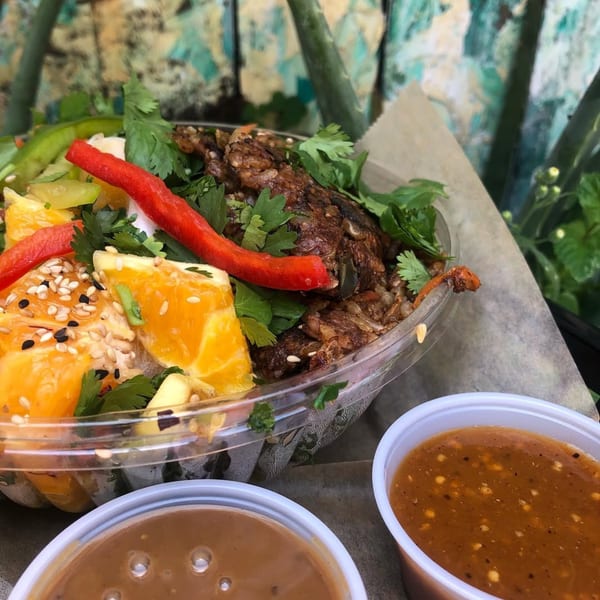 A Tribal Cafe bowl with brown rice, oranges, red peppers, cilantro, and two sauce cups.